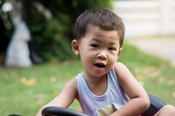 Little boy driving car with the steering wheel. Boy in a white shirt in a red toy car in the street. Little boy driving big toy car and having fun, outdoors.