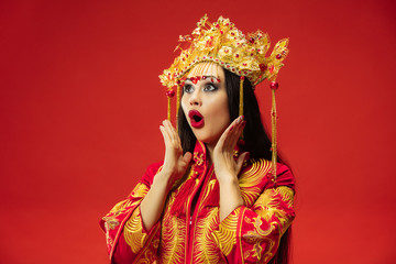 Chinese traditional graceful woman at studio over red background. Beautiful girl wearing national costume. Chinese New Year, elegance, grace, performer, performance, dance, actress, emotions concept