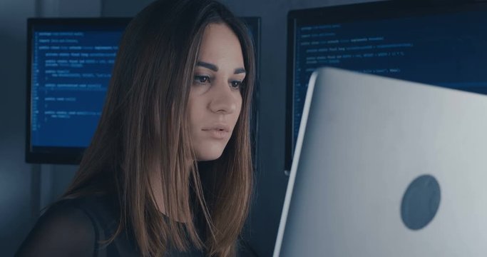 portrait of young woman programmer working at a computer in the data center filled with display screens