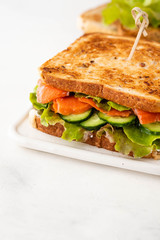 Sandwich with salmon, fresh salad and cucumber on a white board. Copy space.