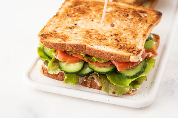 Sandwich with salmon, fresh salad and cucumber on a white board. Copy space.