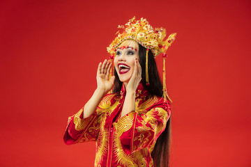 Chinese traditional graceful woman at studio over red background. Beautiful girl wearing national costume. Chinese New Year, elegance, grace, performer, performance, dance, actress, emotions concept