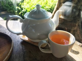 Herbal tea inside white cup and luxury white jar on wooden table. Both are put near glass wall with...