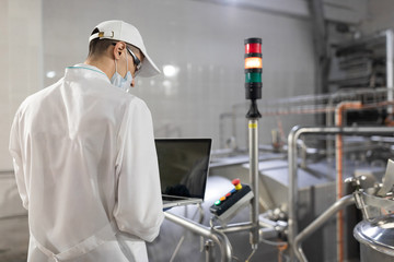 man in a white robe and a mask with a laptop in his hands is at the factory