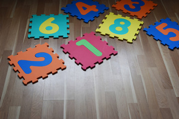 Numbers puzzle pieces different vibrant color on brown wooden texture laminate floor indoors. Educational children toys for learning shapes, colors and numbers concept.