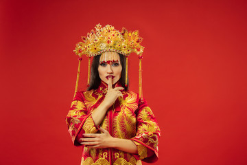 Chinese traditional graceful woman at studio over red background. Beautiful girl wearing national costume. Chinese New Year, elegance, grace, performer, performance, dance, actress, dress concept