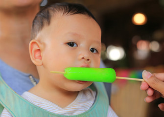 Adorable Asian baby boy sucking ice-cream by people hand.