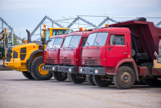 Multiple cars, trucks, loaders, concrete mixers and construction machinery in large parking lot in industrial territory, next to concrete and asphalt factory   