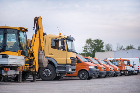 Multiple cars, trucks, loaders, concrete mixers and construction machinery in large parking lot in industrial territory, next to concrete and asphalt factory   
