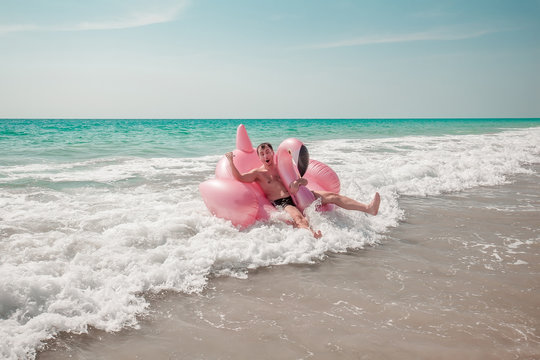 A Man Is Having Fun On Pink Flamingo Inflatable Pool Float In The Turquoise Sea With White Waves