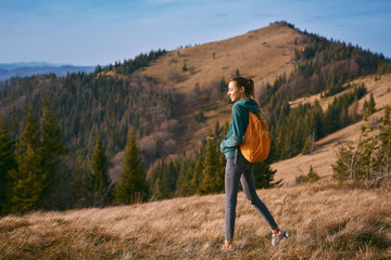 Naklejka na ściany i meble image of a happy woman hiker standing on the slope of mountain ridge on the mountains and blue sky background. the woman is happy and looks around with delight