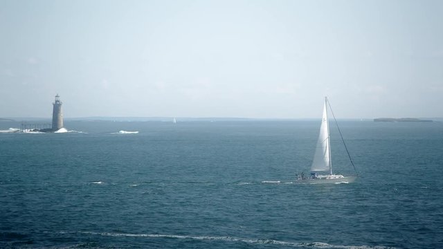 Sailboat passing the Ram Island Ledge Light Station in Casco Bay near Portland, Maine on a nice summer day with blue water
