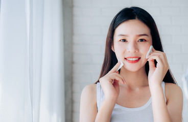Young Beauty Asian Woman Cleaning Face with Cotton Clear Face Skincare and Smile Morning in White Bedroom,Copy Space.