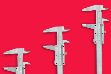 Row of three metal vernier calipers on red table with copy space for your text. Top view. Industrial concept