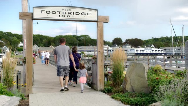 Tourists walking under the entrance archway and to the pedestrian foot bridge in Boothbay Harbor, Maine on a nice summer day with beautiful clouds in the sky. 