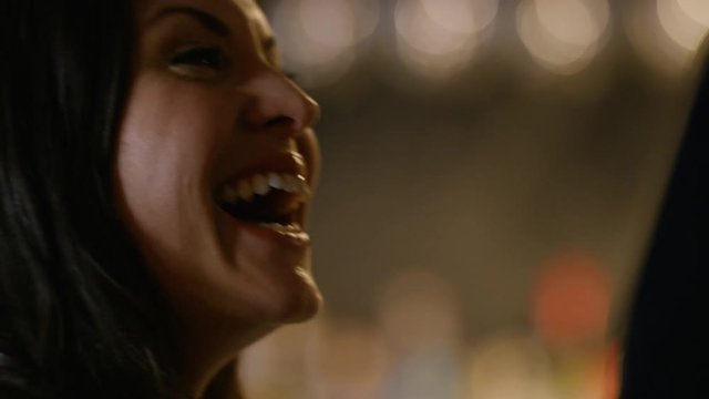 Profile of young brunette female in a bar drinking wine and talking to someone next to her