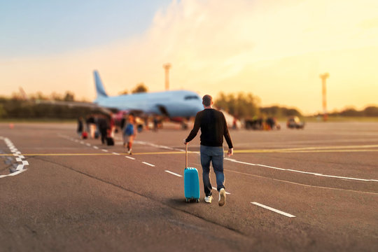 Man tourist passager getting in to airplane at airport, walking from the terminal to the plane.