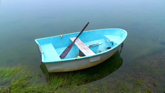 Dinghy rowboat at anchor in a quiet foggy cove.  Camera zooms into oar.