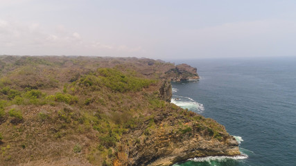Fototapeta premium aerial view rocky coastline with cliffs, ocean surf with breaking waves in coast. seascape waves break on rocky shore java, indonesia