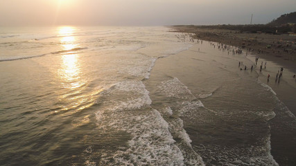 sandy beach parangtritis near ocean with big waves, people in tropical resort at sunset. Yogyakarta, Indonesia. aerial view seascape, ocean and beautiful beach. Travel concept. Indonesia, jawa