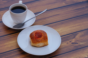 fresh homemade bun with jam and a cup of coffee on a wooden table