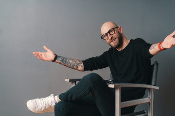 You are always welcome. Man with glasses gesturing and smiling while standing against grey...