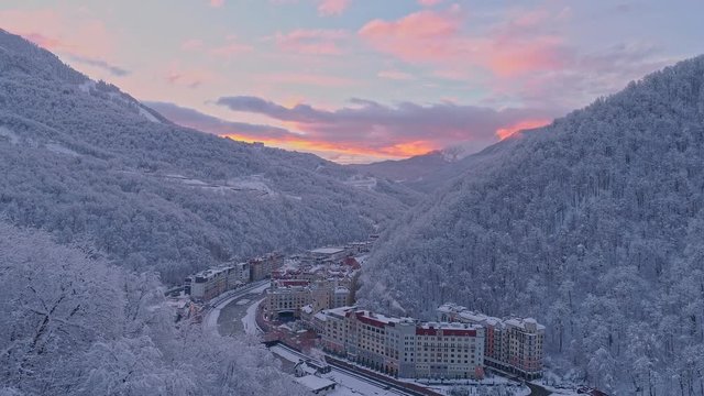 Aerial drone shot of winter Rosa Khutor ski resort during rose sunset in mountains.White winter, snow covered forest.