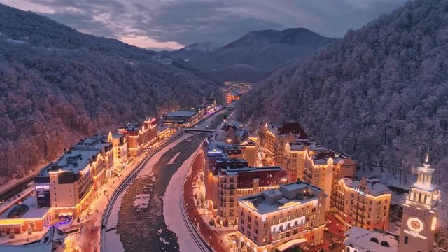 Aerial drone wide shot Evening Rosa Dolina Ski Resort in Sochi Caucasion mountains, Russia. Winter white, snow covered forest