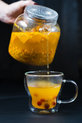 the chef pours sea buckthorn tea in a Cup on black background