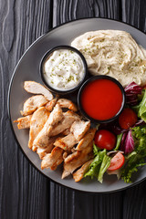 Healthy shawarma plate with chicken, hummus, salad and sauces close-up on a table. Vertical top view
