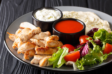 Chicken shawarma with hummus, vegetables and sauce serving on a plate close-up. horizontal