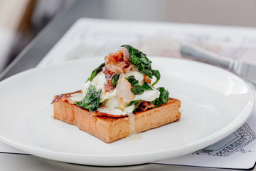 Eggs benedict with brioche, bacon and spinach.