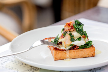 Eggs benedict with brioche, bacon and spinach.