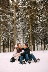young couple having fun in winter park with their dog. Hugging young couple in love walking with dog outdoors in snowy winter