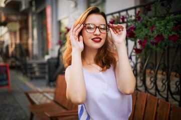 Attractive redhaired woman in eyeglasses posing at street of spring city.