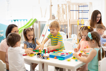 Kindergarten children playing toys with teacher in playroom at preschool. Education concept.