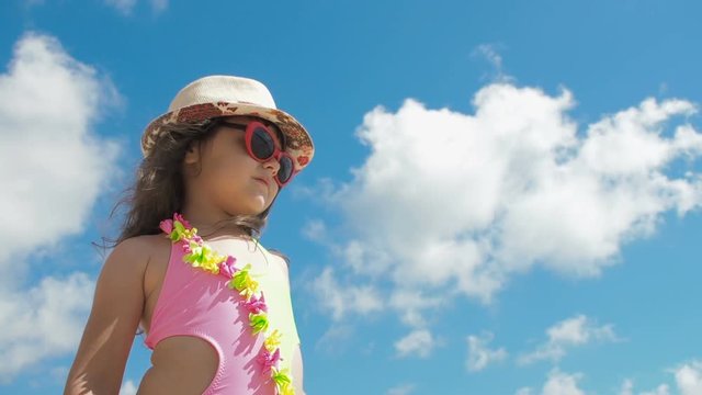 Kid at beach. Cute little girl in a swimsuit, sunglasses and a hat on a background of blue sky.