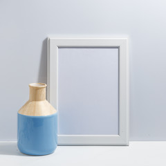Mock up white frame and dry cotton twigs in vase on book shelf or desk. White-blue colors. Minimalistic concept.