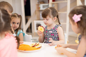 Group of kids have a lunch in daycare centre. Children eating fresh fruits in kindergarten