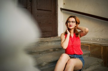 Attractive redhaired woman in eyeglasses, wear on red blouse and jeans skirt posing.