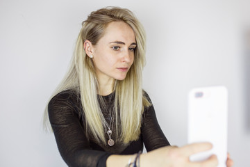 Naklejka premium Girl making selfie on smartphone, against a white wall