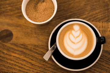 Cup of hot cappucino in a blak cup with coffee art on wooden table background. Hippster style