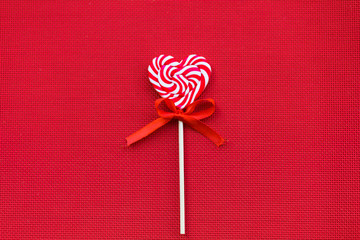 Red sweet lollipop in the shape of a heart on a red background.