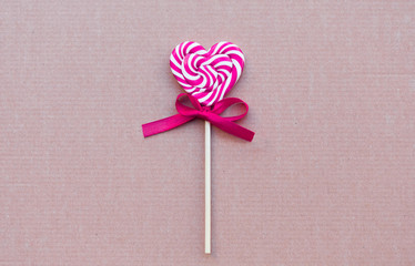 Pink and white candy lollipop in the shape of a heart on a red background.