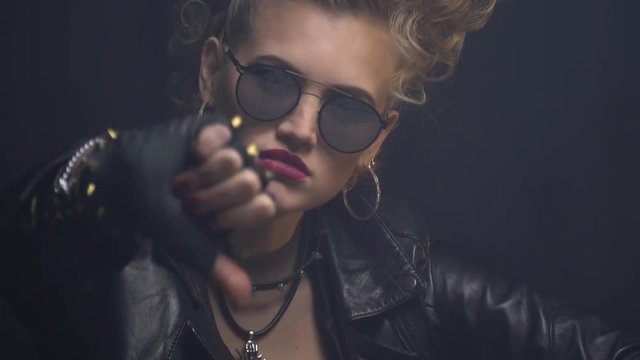 Thumb down by a woman in leather jacket, spiked gloves and sunglasses, close up