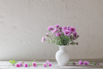violet flowers in white vase on old background