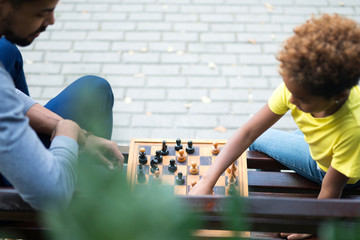 Top view of father and daughter playing chess on the bench in city park. Family leisure time.