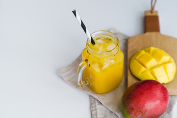 Mango juice in a glass mason jar and mango on a wooden board, white background, space for text