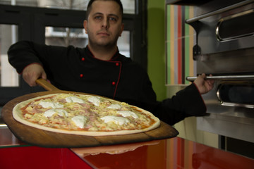 Pizza Master in black uniform put pizza in his stainless steel stove - Image
