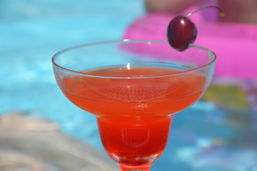 Tasty red cocktail background swimming pool. Margarita cocktail with a glass of cherries.